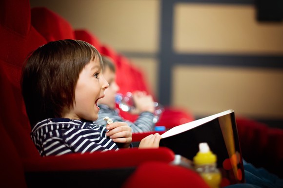 Two children, eating popcorn and watching a movie at the theater.
