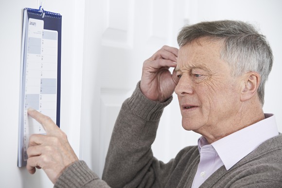 Senior man scratching his head and looking at a wall calendar