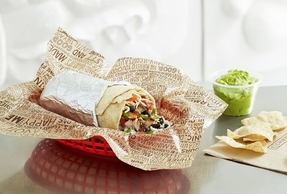 Chipotle burrito in a basket on a table with a side of guacamole and some chips