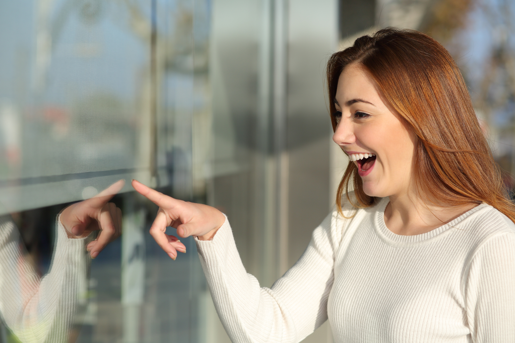 A young woman points at a store window with a big smile.