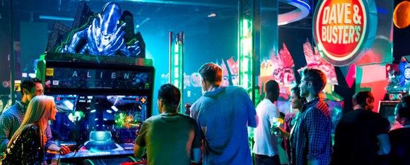 A group of adults gather around the arcade game Alien, based on the popular sci-fi movies, at a Dave and Buster's.
