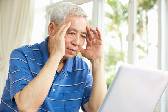 Senior man holding his head while looking at a laptop