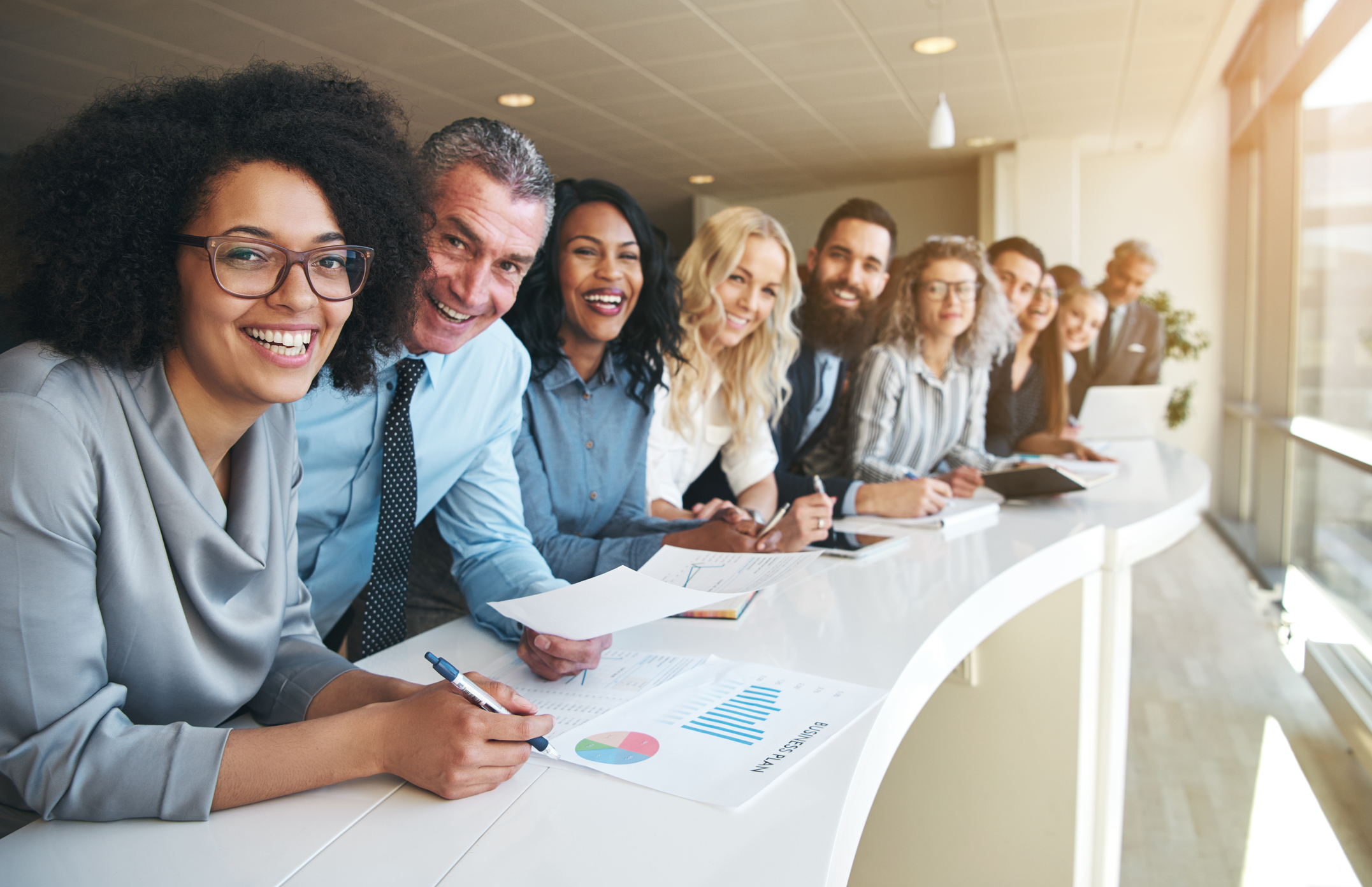 Line of smiling professionals leaning against a desk