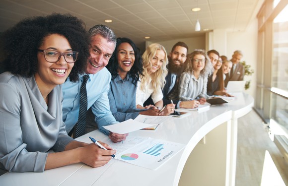 Line of smiling professionals leaning against a desk