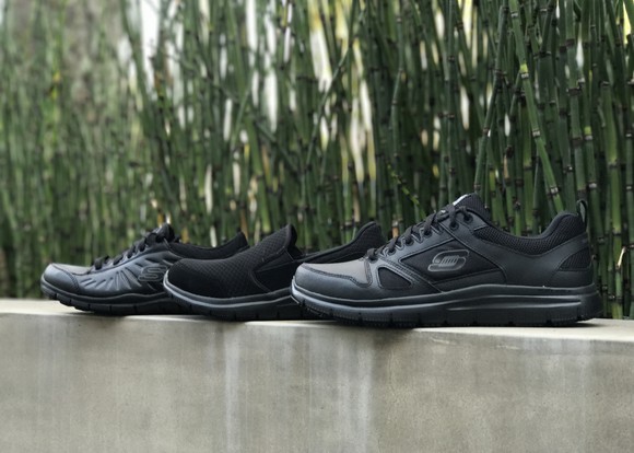 Three Skechers shoes on a concrete wall, with plants in the background.