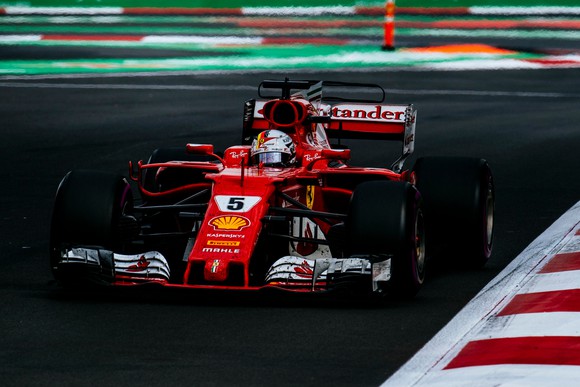 A Ferrari race car driven by Sebastian Vettel is shown at speed on a racetrack.