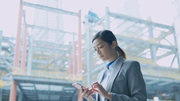 A woman checking her phone with industrial scaffolding in background.