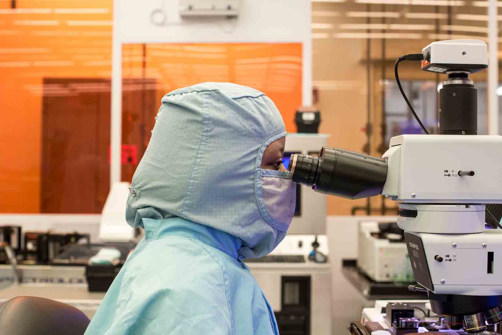 A Finisar employee in a clean suit looking into a microscope