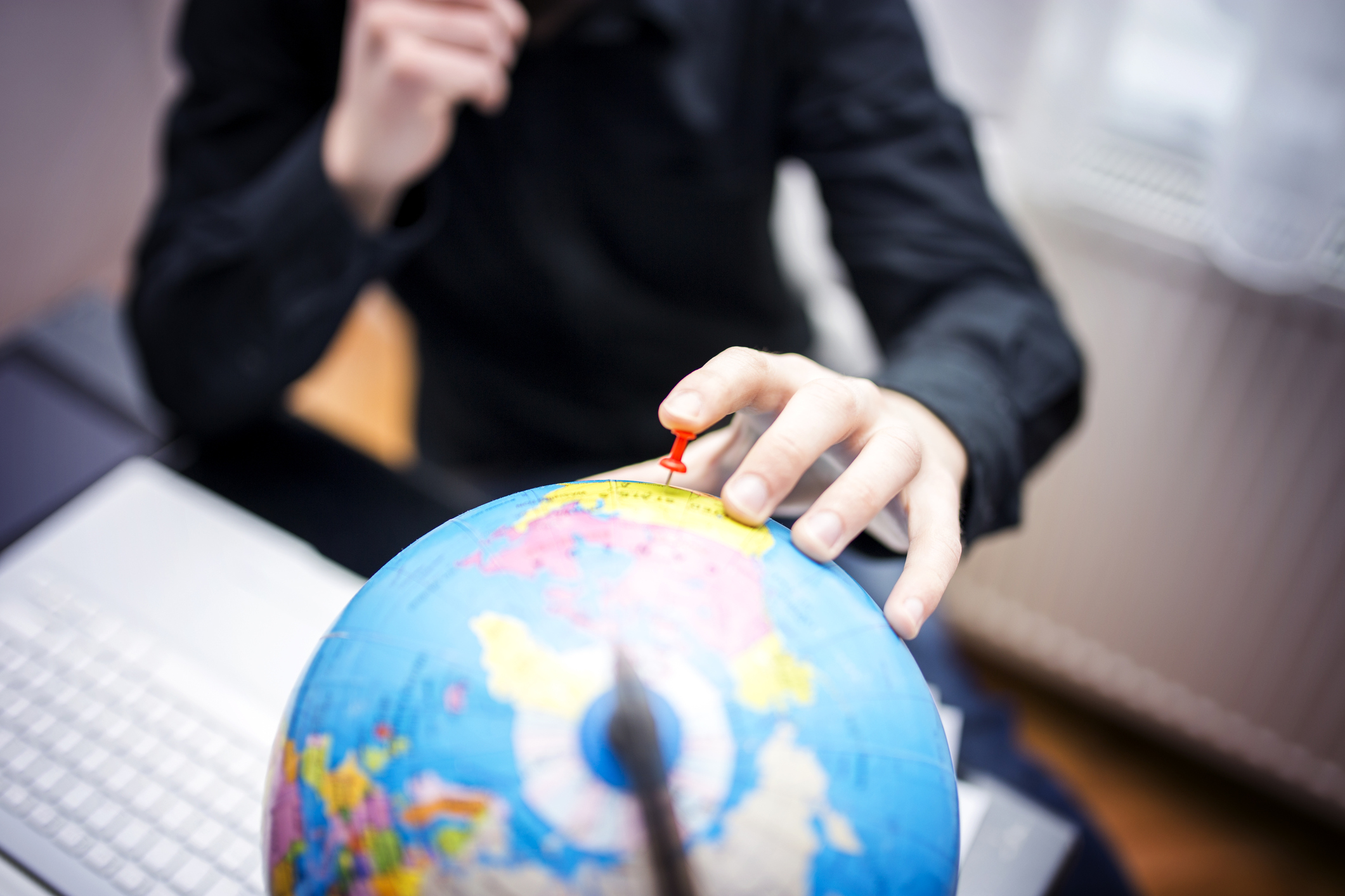 A person sticks a pin in the United States on a globe.
