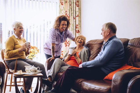 Group of seniors hanging out while a woman in scrubs smiles and talks to them