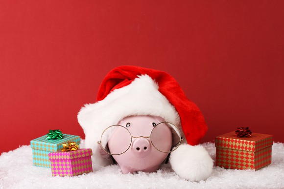 A piggy bank with spectacles and a Santa hat with gifts next to it.