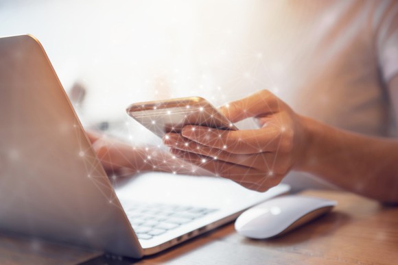 Woman using connected cell phone and computer. 