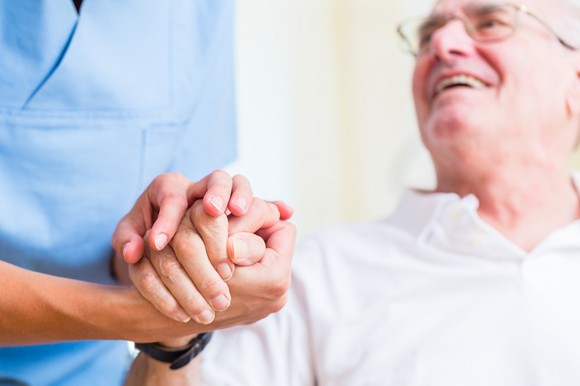 An elderly man holds hands with a smiles at his caregiver.