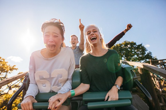 Young adults smiling while riding a roller coaster.