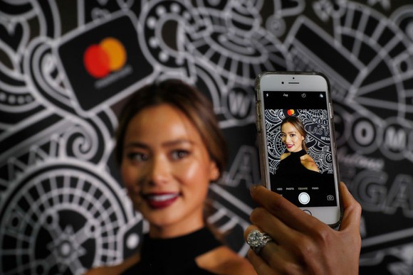 Female taking selfie in front of Mastercard logo and graphic designs on wall.