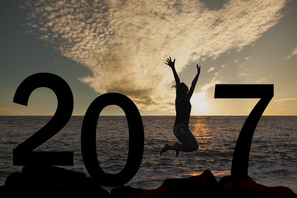 Silhouette of 2017 at sunset in front of ocean with woman jumping where the 1 would be