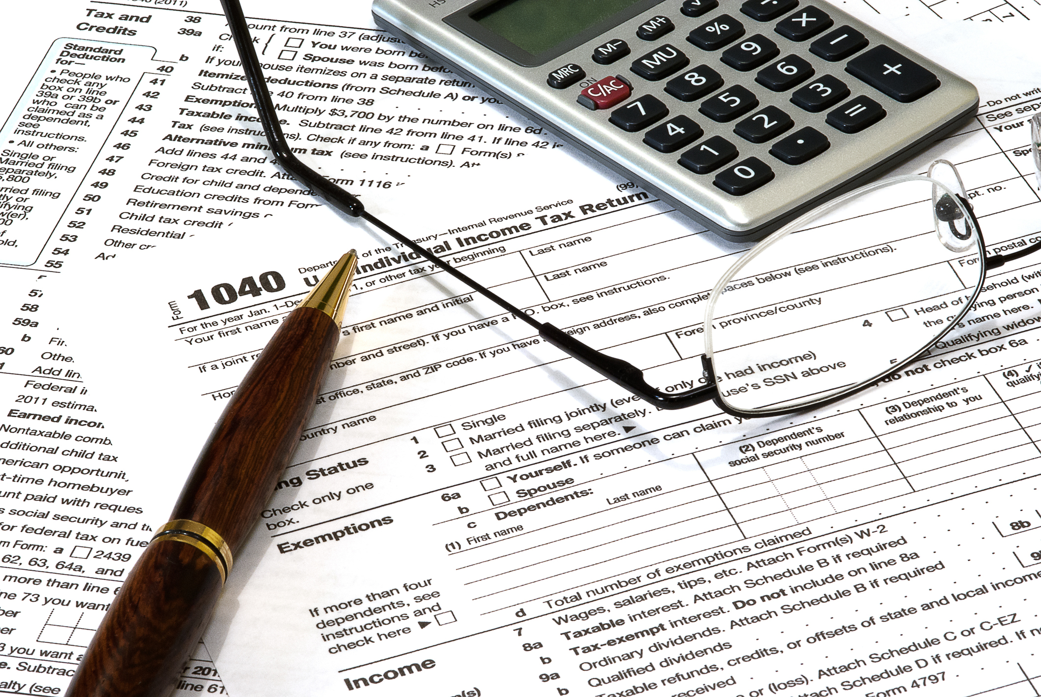 A pen, glasses, and calculator sitting on a 1040 tax form.