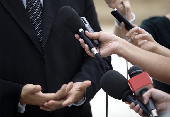 People pointing microphones at a man in a suit