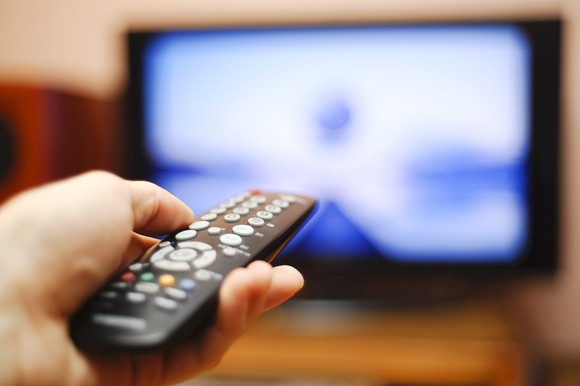 A hand points a remote at a television.