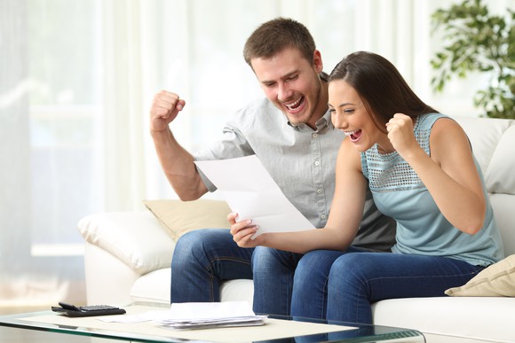 A millennial couple sitting on a couch happily as they read a piece of paper.