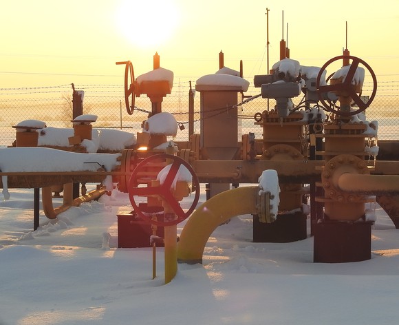 Snow covered pipes coming from a natural gas field with the sun in the distance.