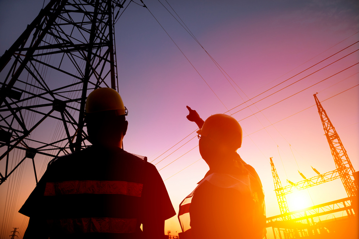 Two utility workers looking up at power transmission lines.