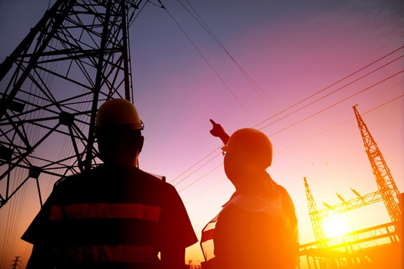 Two utility workers looking up at power transmission lines.