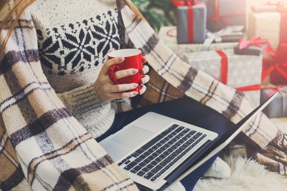 Woman holding mug with an open laptop in her lap.