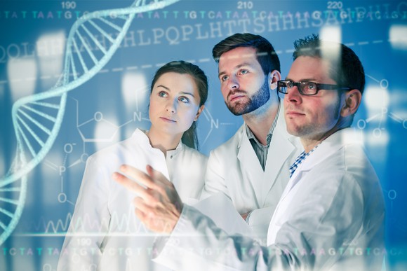 Researchers in lab coats looking at a monitor displaying data and a double helix.