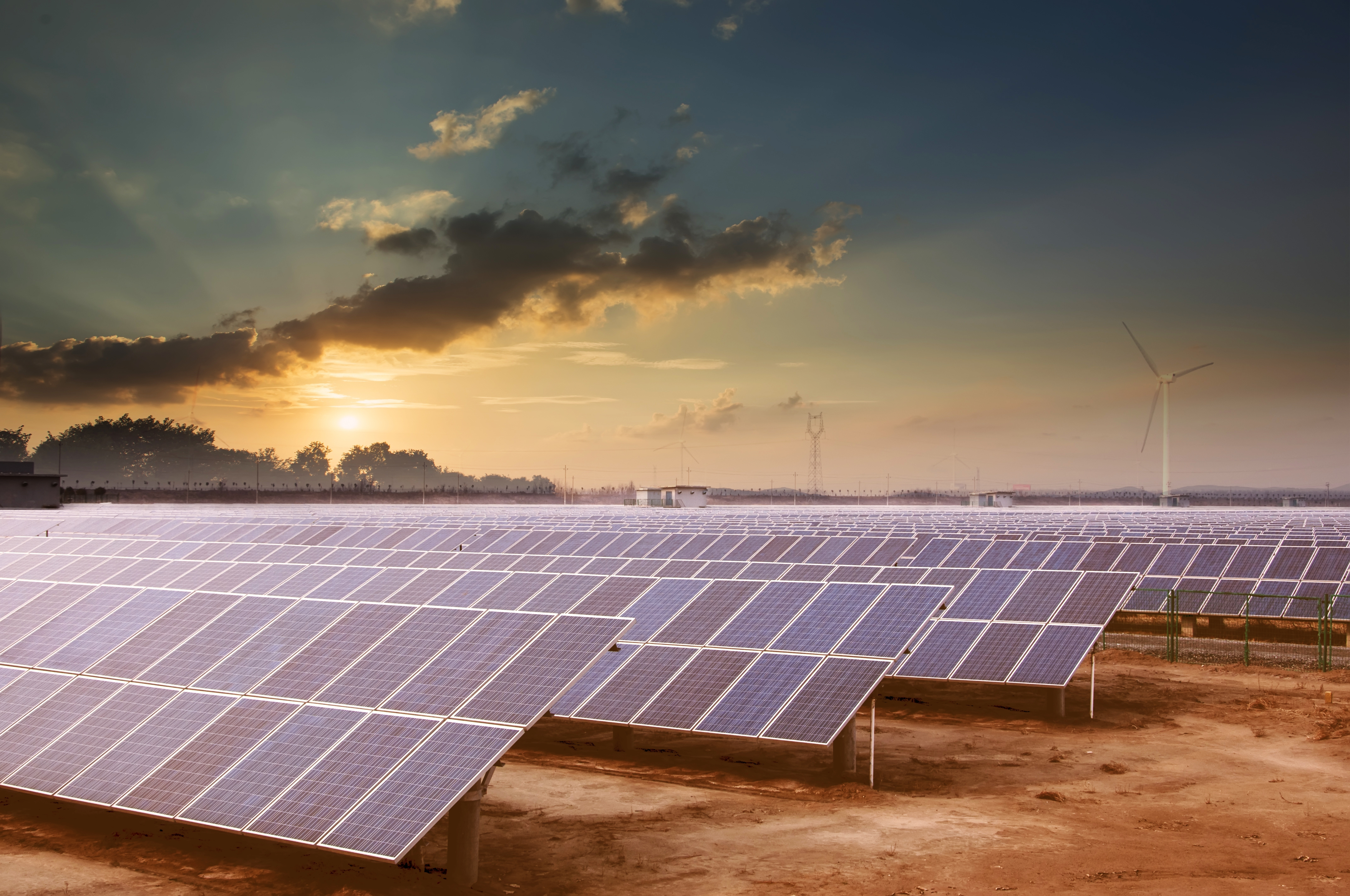 Solar farm in a desert with a setting sun in the background.