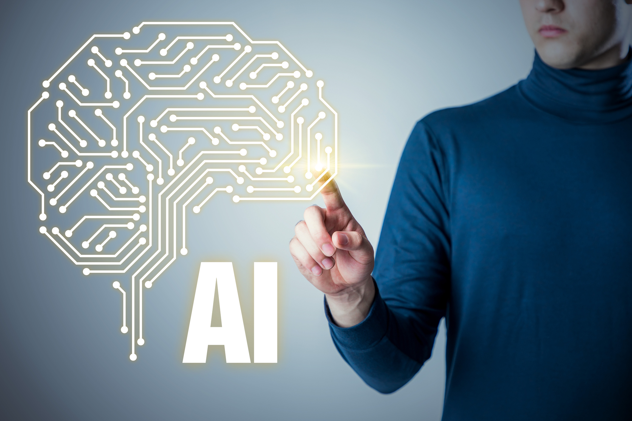 A person in a blue turtleneck pointing to a screen with an image of digital human brain and the letters "AI."