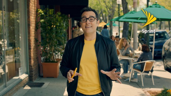 Sprint spokesman Paul Marcarelli walks down a sidewalk with people dining behind him.