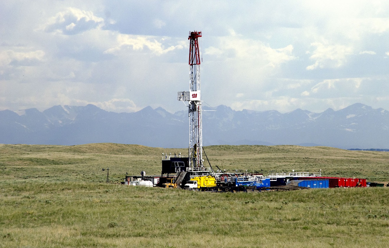 Drilling rig and associated equipment on a pasture with the Front Range and clouds in the background.