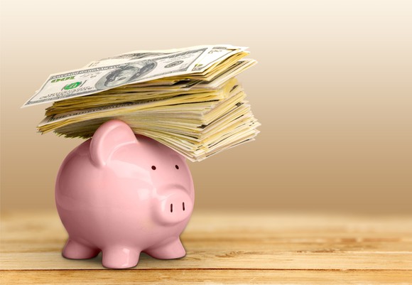 pink piggy bank with a stack of hundred dollar bills resting on top of it