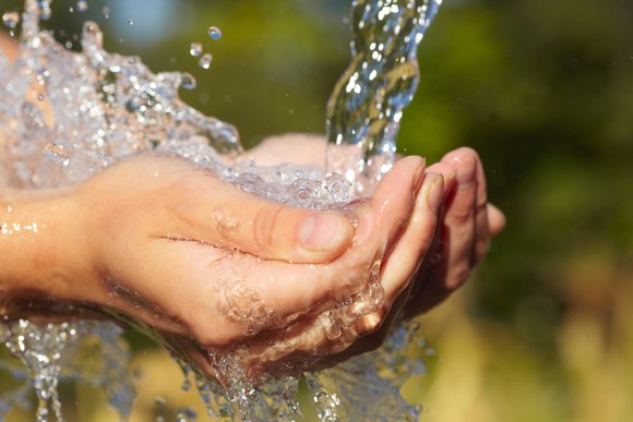 Cupped together, two hands catch falling water.