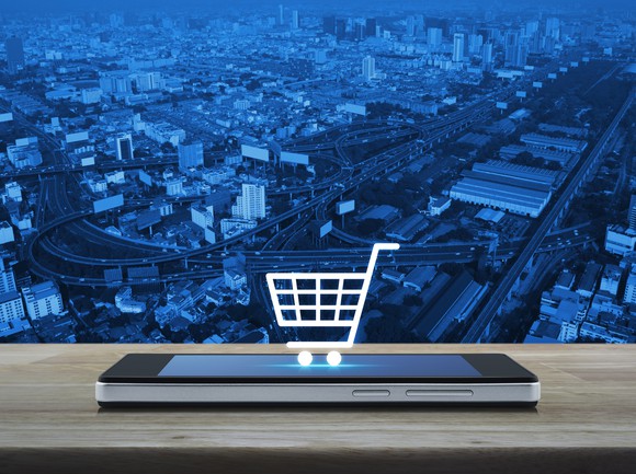A mobile phone displaying a shopping cart icon, with a city landscape in the background.