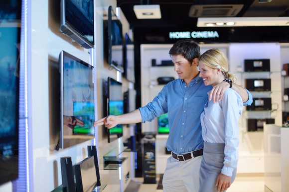 A man and woman in a store looking at a TV.
