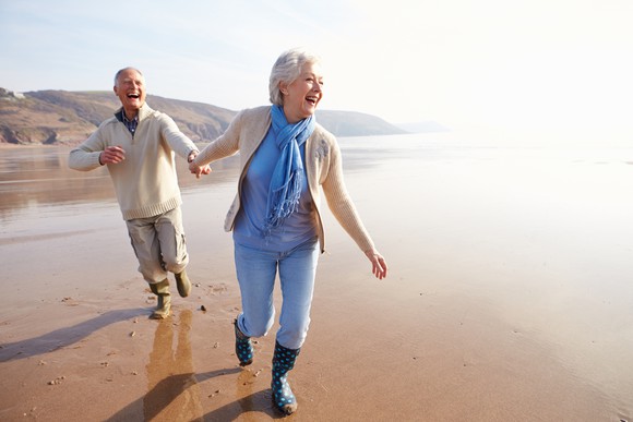 Senior couple holding hands and running along the beach