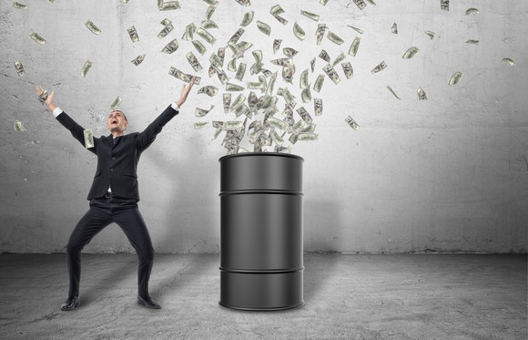 A smiling man raises his arms next to an oil barrel above which is a cloud of paper money.