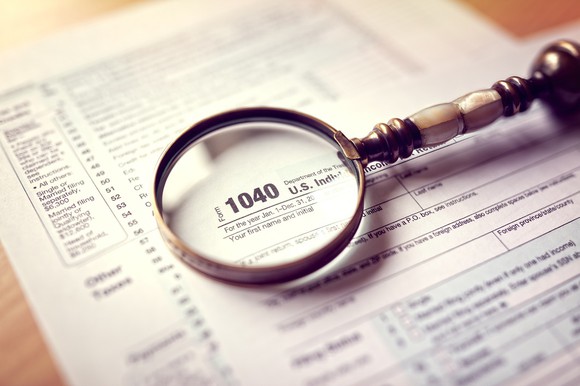 Tax returns on a wood desk with a magnifying glass on top of them.