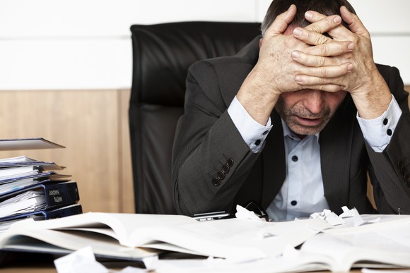 Professionally dressed man holding his head at his desk, as if stressed