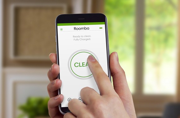 Hand holding a smartphone, pushing a "CLEAN" button on iRobot's mobile app