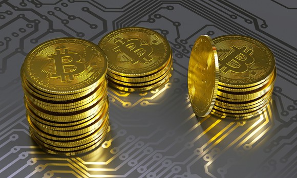 Piles of gold coins marked with the bitcoin label on a table with semiconductor chip circuitry.