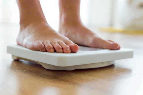 Person standing on a scale, only shown from just above the ankles down.