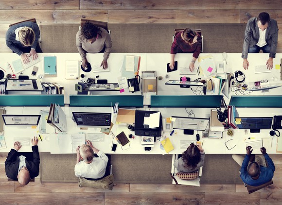 Aerial view of eight workers around a long desk.