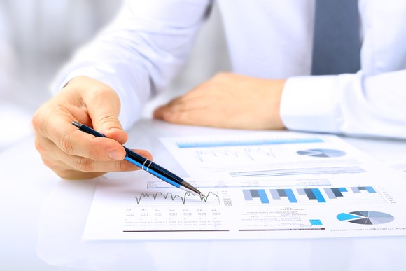 Hand holding a pen on top of a piece of paper with several graphs and charts.
