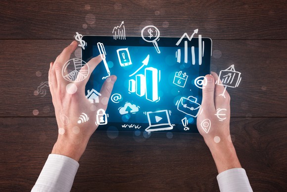 A person holding a tablet around which are icons representing things including money, security, and a house.
