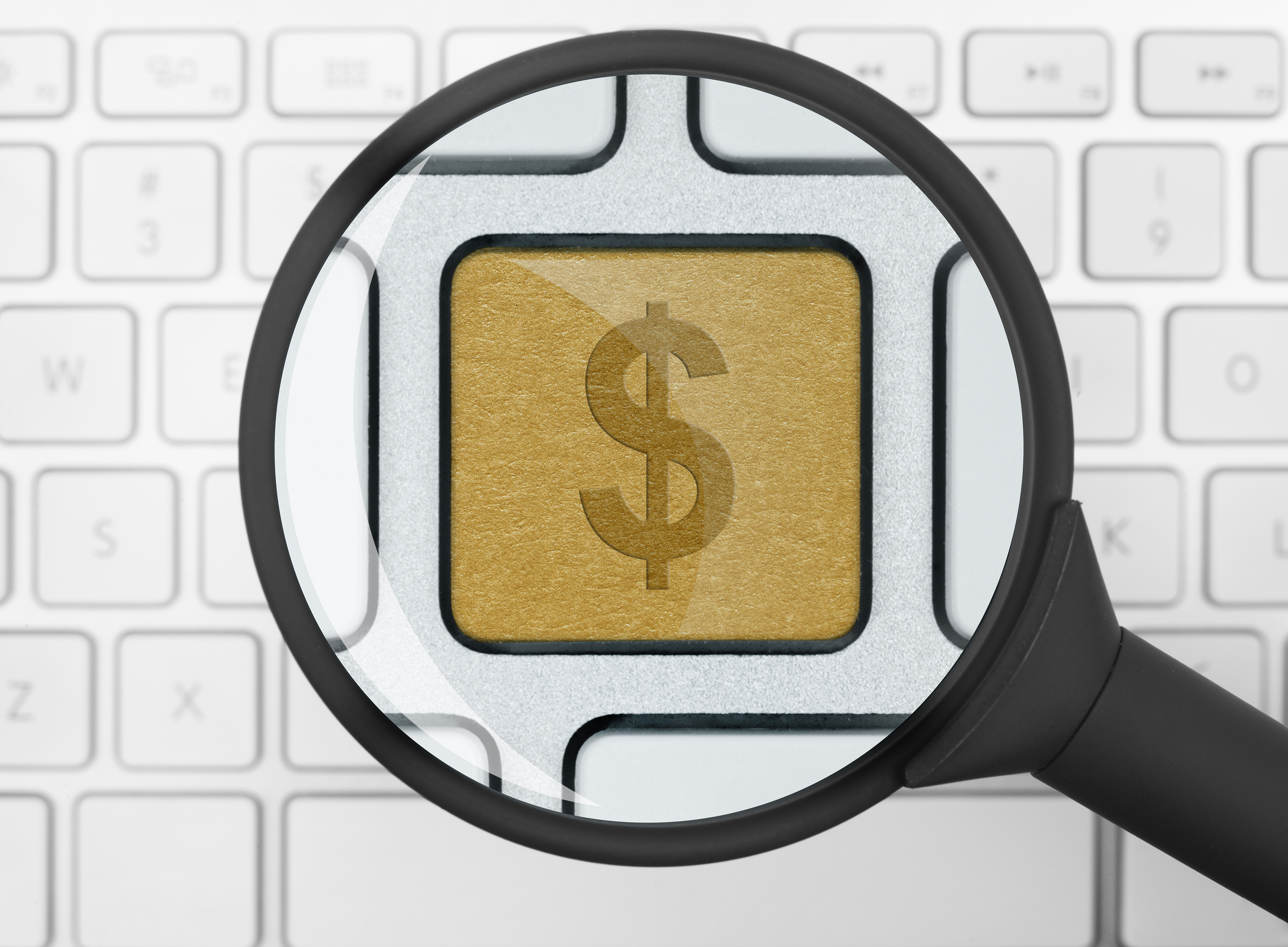 White computer keyboard under a looking glass, and the G key is replaced by a gilded dollar sign.