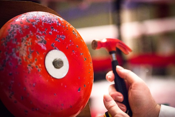 closeup of a red boxing bell and a hand hitting it with a small red hammer.