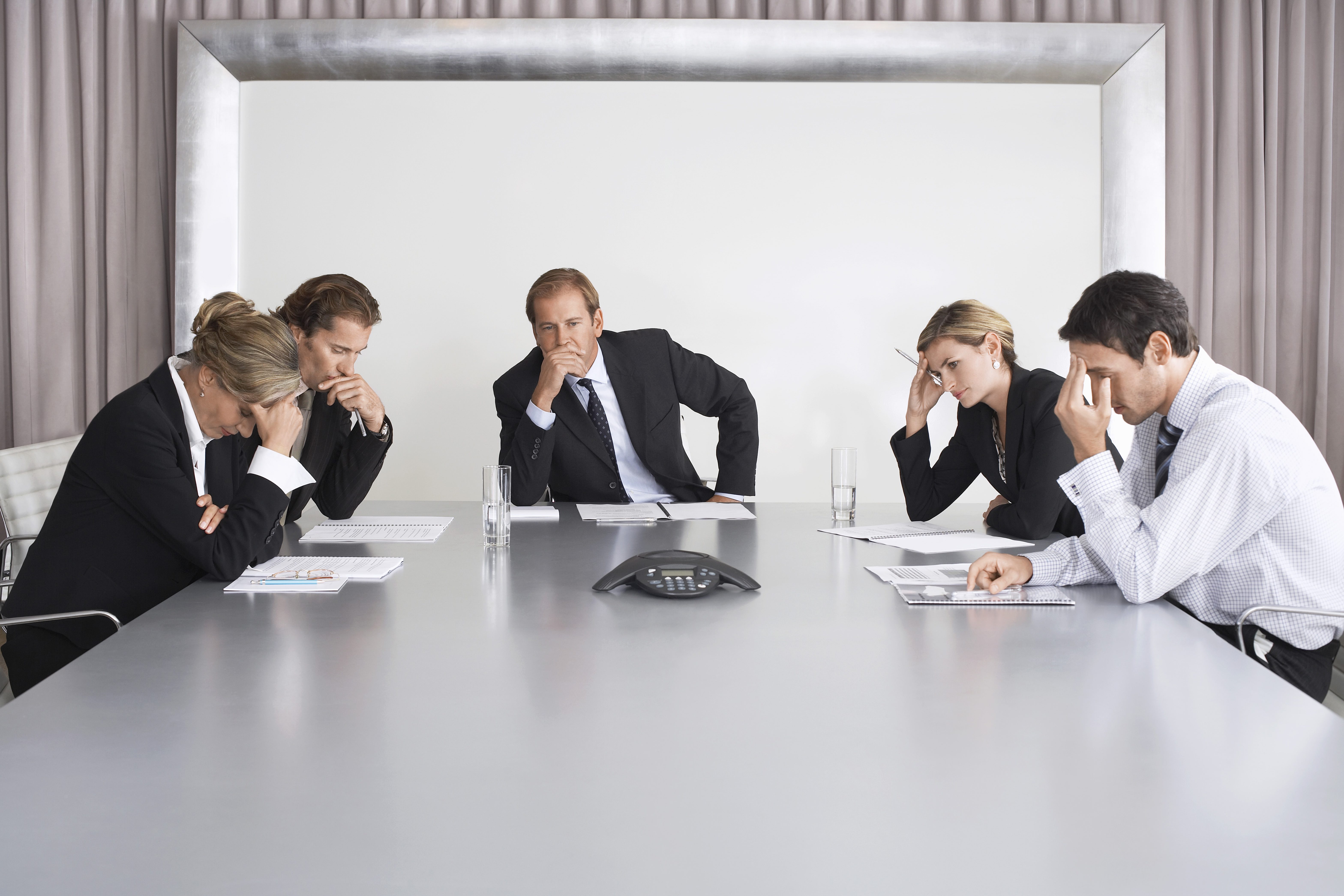 Management team of five people sitting around a conference table looking worried